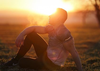 Muscular man sits in rural field at sunset, exhaling visible breath.