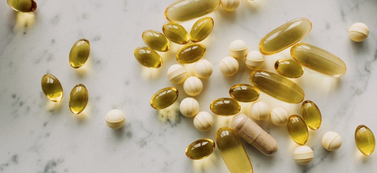 A variety of capsules and pills scattered on a light marble background.