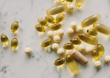 A variety of capsules and pills scattered on a light marble background.